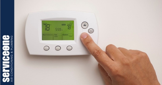 A hand touching a button on a programmable thermostat set to 78 degrees